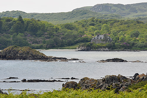 Picture of a house on a wooded shore, seen across skerries