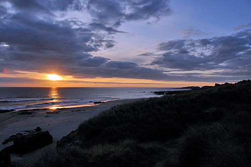 Picture of a cloudy sunset over a bay with a beach and dunes