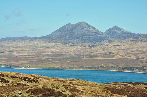 Picture of a view from a hill across a sound to three high mountains