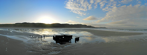 Panoramic picture of a sunrise over a bay with a sandy beach, a wreck in the sand